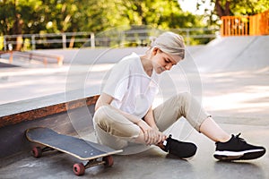 Young skater girl holding her painful leg with skateboard near at skatepark