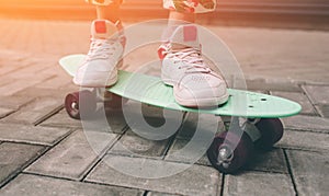 Young skater girl in pink slip on shoes ride colorful tiny skateboard deck outdoors in summer.Sunlight and warm weathe