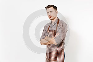 Young skeptic upset man chef or waiter in striped brown apron, shirt holding hands folded isolated on white background