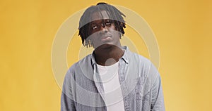 Young skeptical african american man with dreadlocks rolling up his eyes and shaking head in negation, orange background