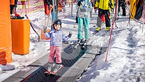 Young skier girl going up on conveyor lift belt to learn how to ski