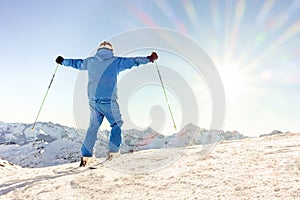 Young skier at the top of mountain raising arms at sky for goal achieved - Sporty man enjoying skiing day with sun light in