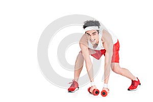 Young skinny man in jogger shoes and shorts with dumbbells