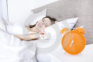 Young sleeping woman and alarm clock in bedroom at home