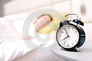 Young sleeping woman and alarm clock in bedroom at home