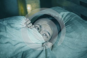 Young sleepless beautiful and scared Asian Japanese woman lying on bed awake at night suffering nightmare after watching zombie