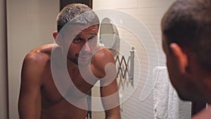 A young sleepy man is washing himself in the bathroom in front of a mirror