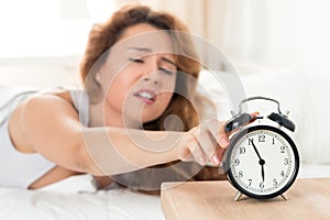 Young sleepy woman trying to turn off the alarm clock