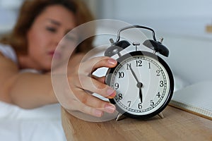 Young sleepy woman trying to turn off the alarm clock
