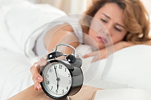 Young sleepy woman trying to turn off the alarm clock