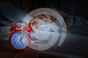 Young sleepy woman is waking up at morning and is turning off alarm clock