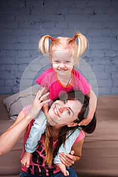 A young slender beautiful mother with her blond daughter on her shoulders play, enjoy and indulge in the teams near the sofa on th