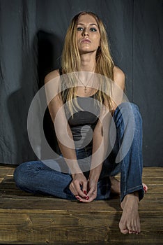 Young slender blonde girl in jeans and shirt posing coquettishly