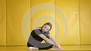 Young slender girl in black clothes is sitting in studio. Yoga class in room.