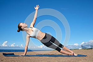 Young slender girl doing yoga on the beach on a sunny morning, plank exercise, healthy lifestyle