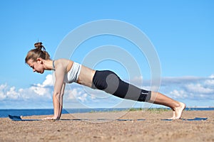 Young slender girl doing yoga on the beach on a sunny morning, plank exercise, healthy lifestyle