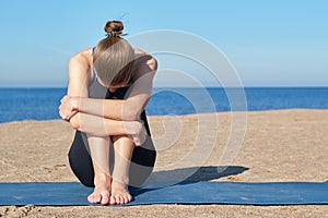 Young slender girl doing yoga on the beach on a sunny morning, sad mood, sad thoughts