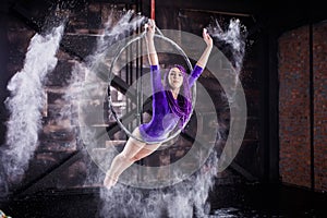 A young, slender girl in a lavender leotard and lilac dreads, doing gymnastics on the air ring, the Hoop and throws the