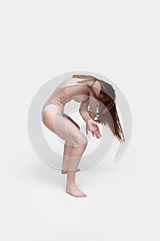 Young slender girl, with long hair, in a beige bodysuit, in the studio on a white background