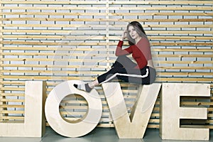 Young slender girl sits on a wall background on letters