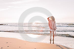 A young slender girl stands alone on the beach or ocean and look at the horizont. A woman dressed in a warm sweater