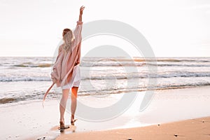 A young slender girl stands alone on the beach or ocean and look at the horizont. A woman dressed in a warm sweater. Warm fall,