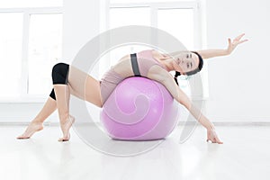 Young slender girl strengthens the back muscles with the help of fitness ball