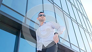 A young slender man against the background of a tall skyscraper looks at the clock.