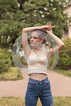 Young slender woman 18 years old stands in park with raised arms.