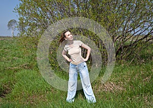 The young slender woman does sporting training at a green bush