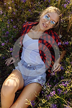 A young slender woman lies in a field among purple wild flowers.