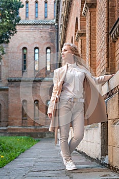 Young slender woman in white clothes near old red brick building looking into the side. Girl alone. Vertical frame
