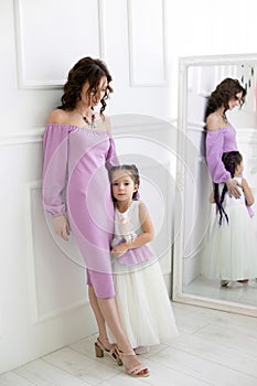 Vertical portrait of a slender young mother and her five year old daughter against the background of the mirror