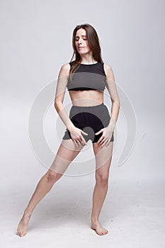 Young slim athletic girl, with long hair, in a black top and shorts, in the studio on a white background