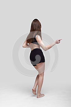 Young slim athletic girl, with long hair, in a black top and shorts, in the studio on a white background