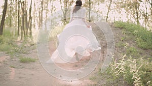 Young slim and attractive girl in elegant white vintage dress with a long fluttering train and flying dark wavy hair in