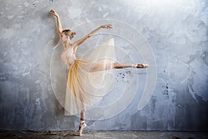 Young ballerina in a golden colored dancing costume is posing in a loft studio