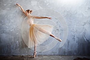 Young ballerina in a golden colored dancing costume is posing in a loft studio