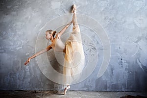 Young ballerina in a golden colored dancing costume is posing in a loft studio