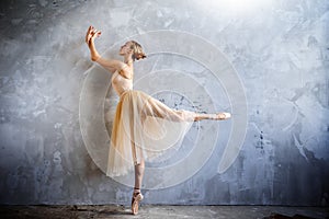 Young ballerina in a golden colored dancing costume is posing in a loft studio