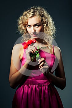 Young slim beautiful blond woman with curly hair in purple dress standing, smiling and looking at camera