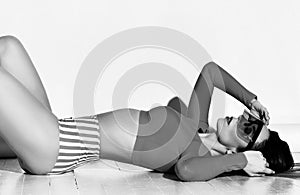 Young slim beautiful sexy woman in striped sportswear and sunglasses lying on floor showing perfect body lines