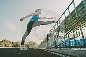 Young slim blond woman at green grass of stadium in the morning making exercises. Healthy lifestyle outdoor. Stretching.