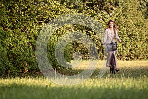 Young, slim, blonde woman on bicycle against defocused park landscape. Autumn color shade