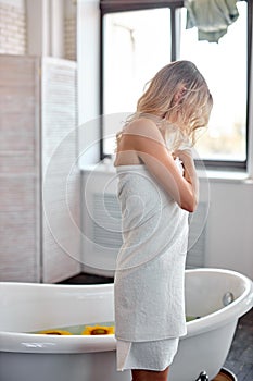 Young slim blonde woman drying body with towel after taking bath, side view