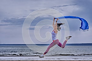 Young slim brunette woman jumping while jogging while holding a blue scarf in her hands. A woman is engaged in gymnastics in the s