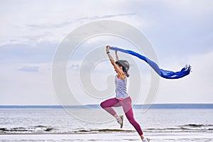 Young slim brunette woman jumping while jogging while holding a blue scarf in her hands. A woman is engaged in gymnastics in the s