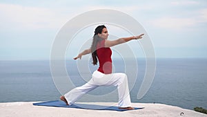 Young slim female doing yoga warrior pose near the sea
