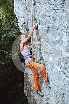 Young slim female rock climber climbing on the cliff