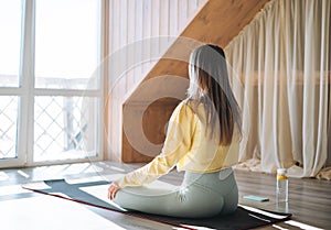 Young slim fitness blonde woman practice morning yoga near the window of home